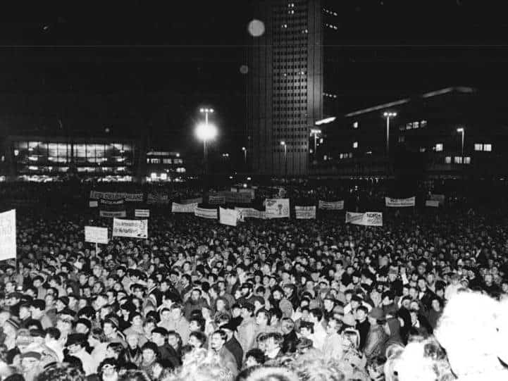 Schwarz-Weiß-Aufnahme einer Montagsdemonstration in Leipzig 1989: eine riesige Menschenmenge mit Transparenten bei Nacht