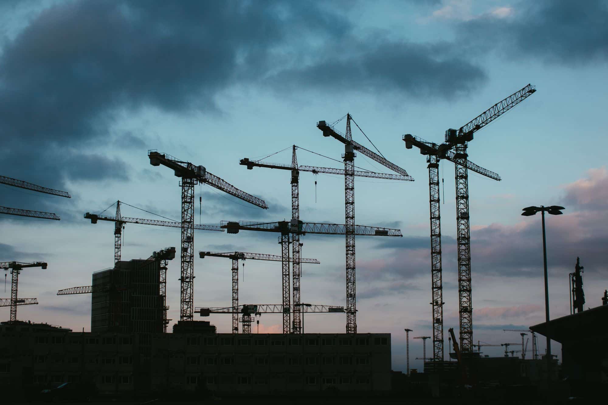 Silhouetten von Baukränen über einer Stadtkulisse in der Abenddämmerung